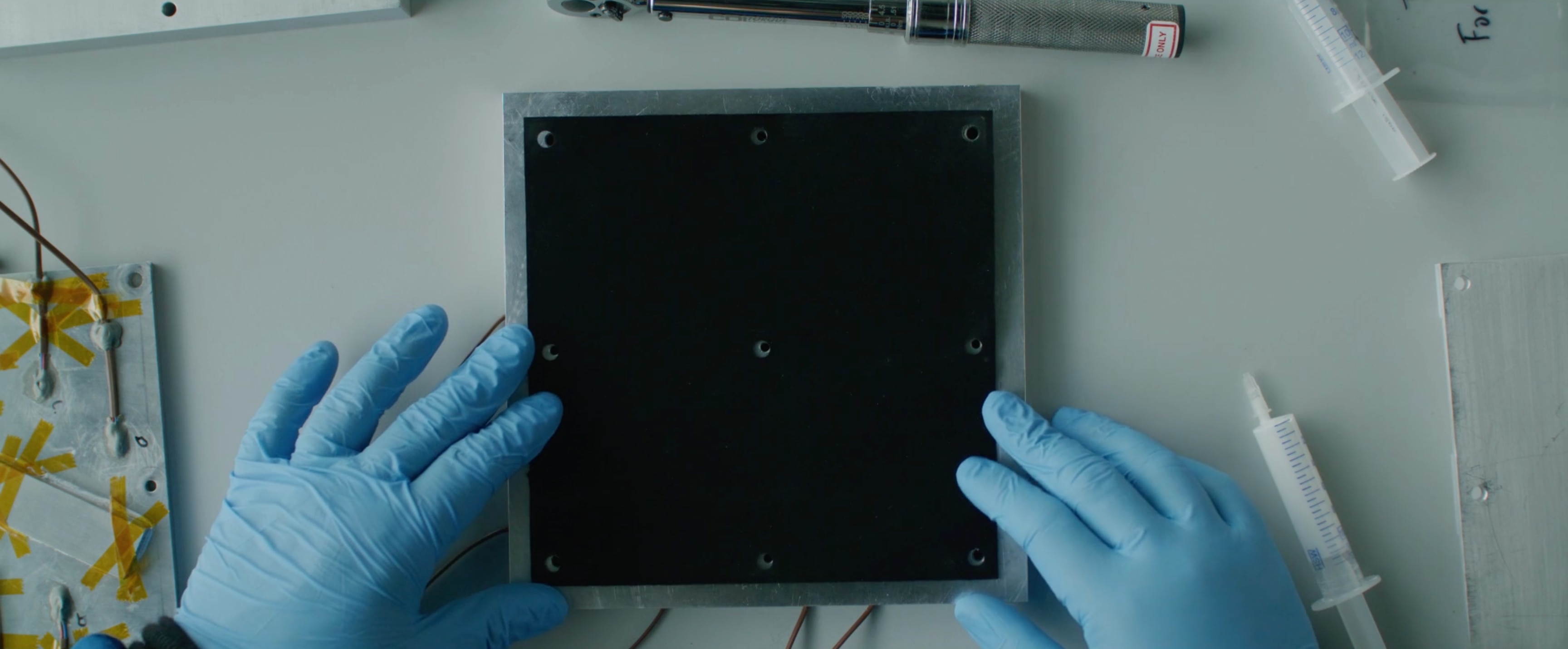 Gloved hands working with conductive materials on a lab workstation.